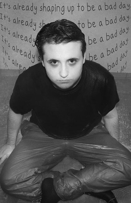 A black and white image of a man sitting in a puddle and looking up at the camera.